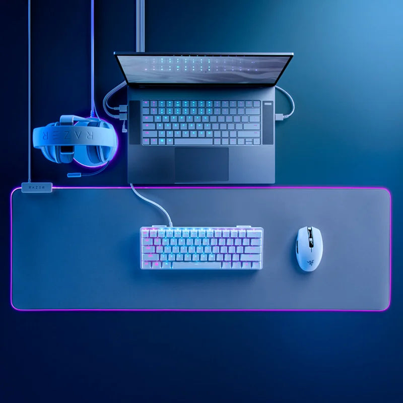 Gaming setup with laptop, keyboard, mouse, and VR headset on a dark surface with blue lighting.