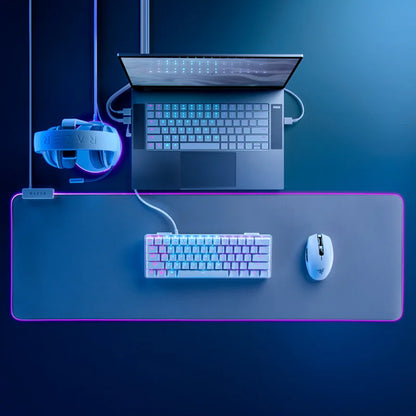 Gaming setup with laptop, keyboard, mouse, and VR headset on a dark surface with blue lighting.